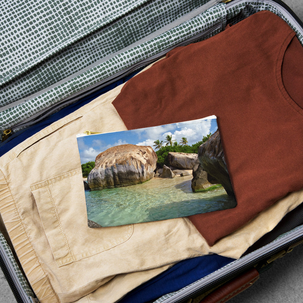 Small pouch with calm turquoise water design lying flat atop the contents of an open suitcase.