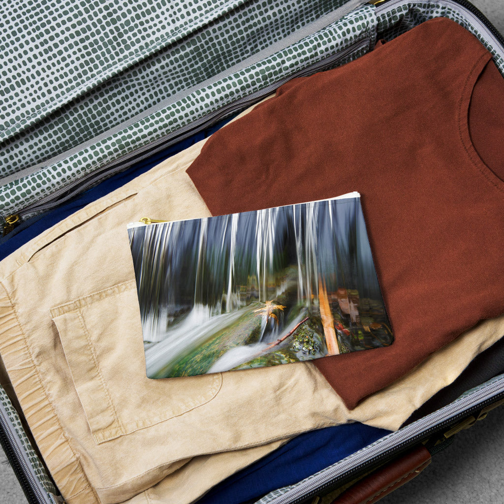 Small pouch with creek waterfall design lying flat atop the contents of an open suitcase.