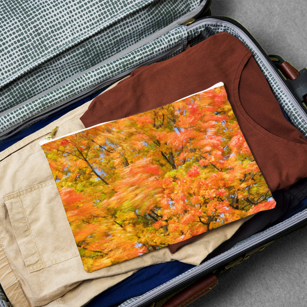 Large pouch with fall colored trees design lying flat atop the contents of an open suitcase.
