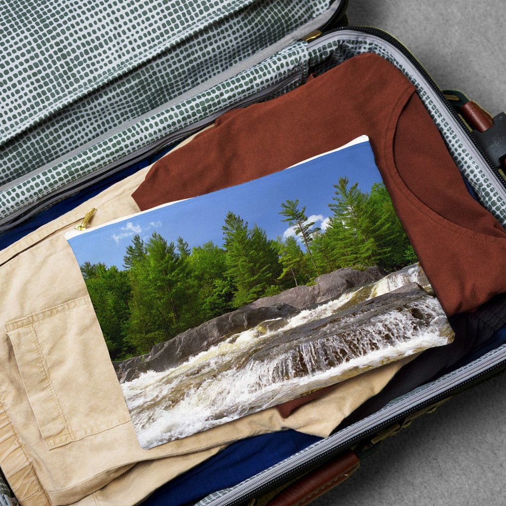 Large pouch with forest waterfall design lying flat atop the contents of an open suitcase.