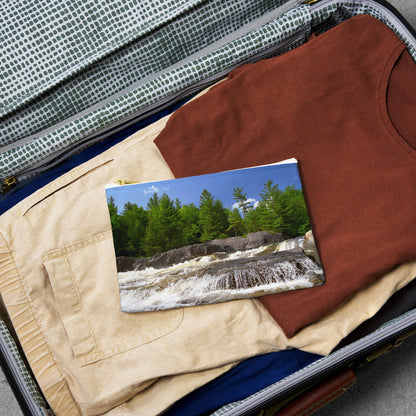 Small pouch with forest waterfall design lying flat atop the contents of an open suitcase.