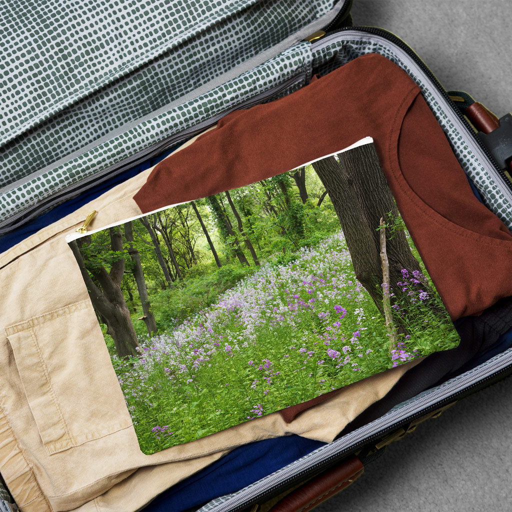 Large pouch with forest wildflowers design lying flat atop the contents of an open suitcase.