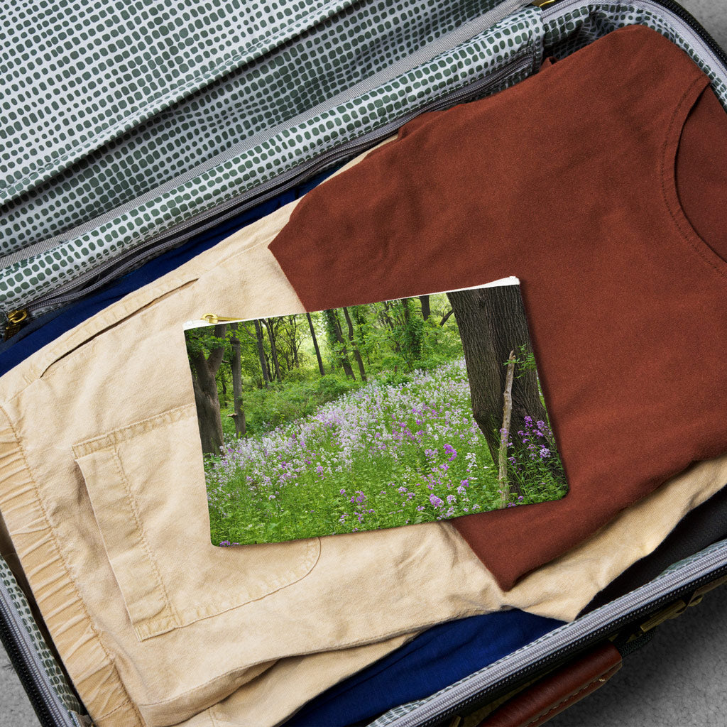 Small pouch with forest wildflowers design lying flat atop the contents of an open suitcase.