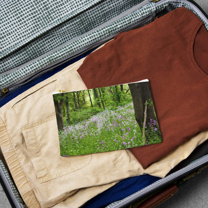 Small pouch with forest wildflowers design lying flat atop the contents of an open suitcase.