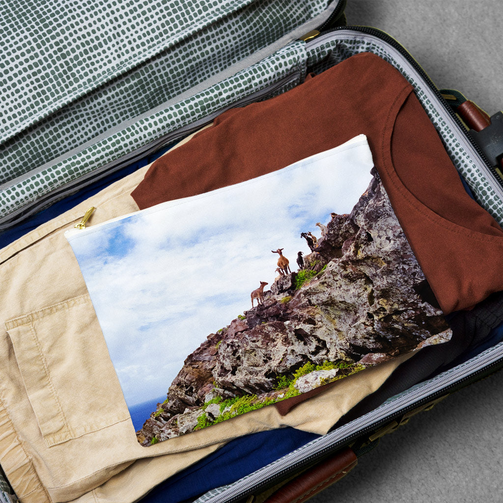 Large pouch with curious goats design lying flat atop the contents of an open suitcase.