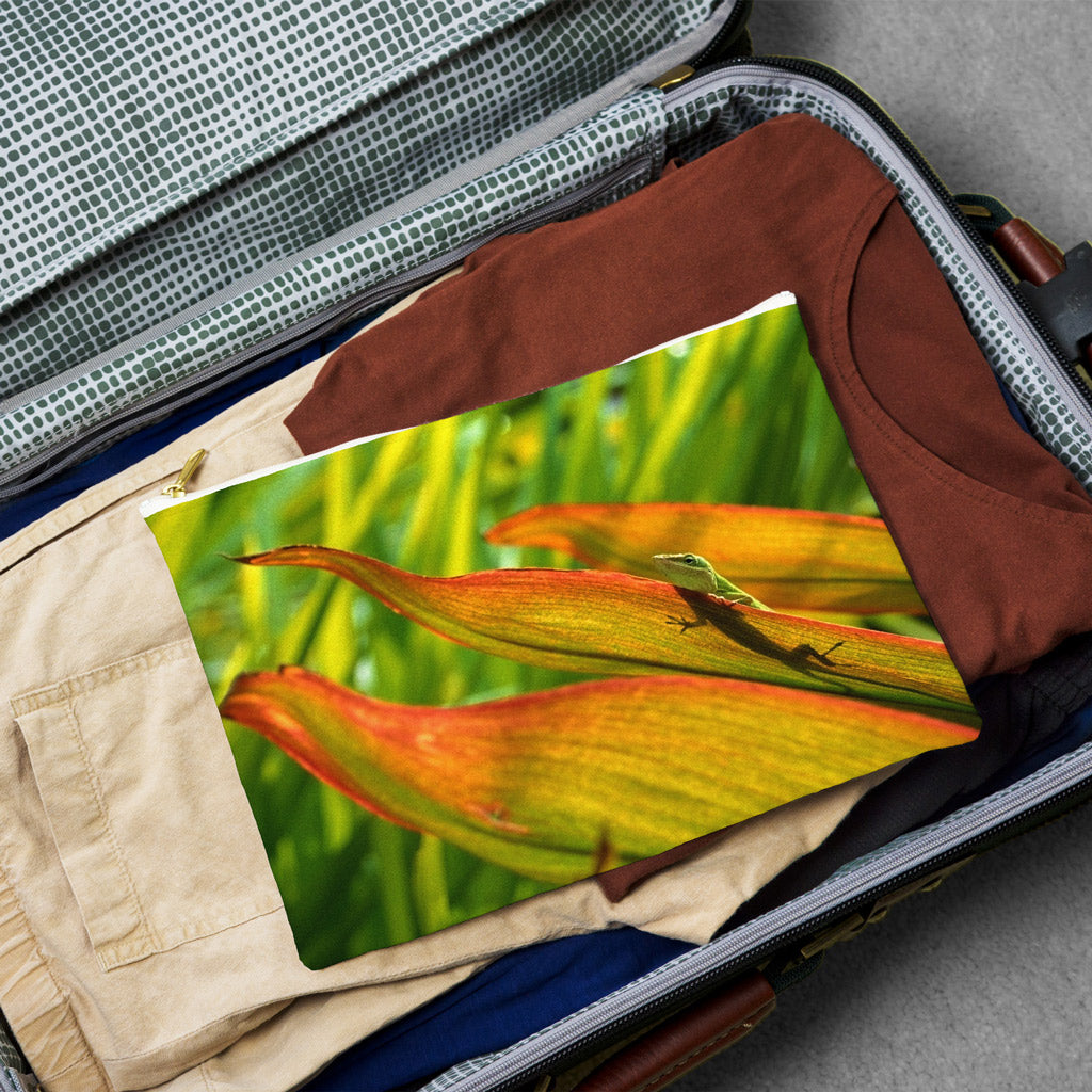 Large pouch with sunlit gecko design lying flat atop the contents of an open suitcase.