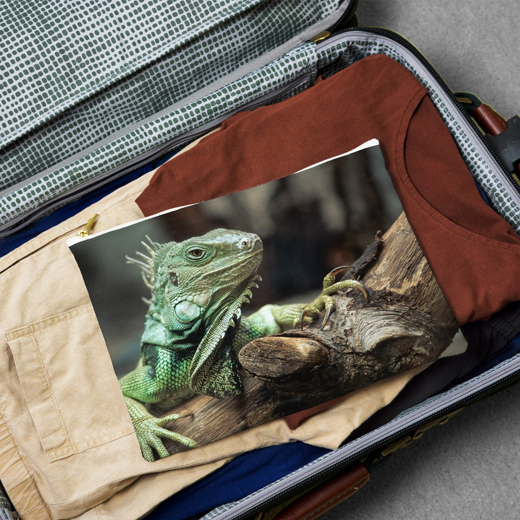 Large pouch with green iguana design lying flat atop the contents of an open suitcase.
