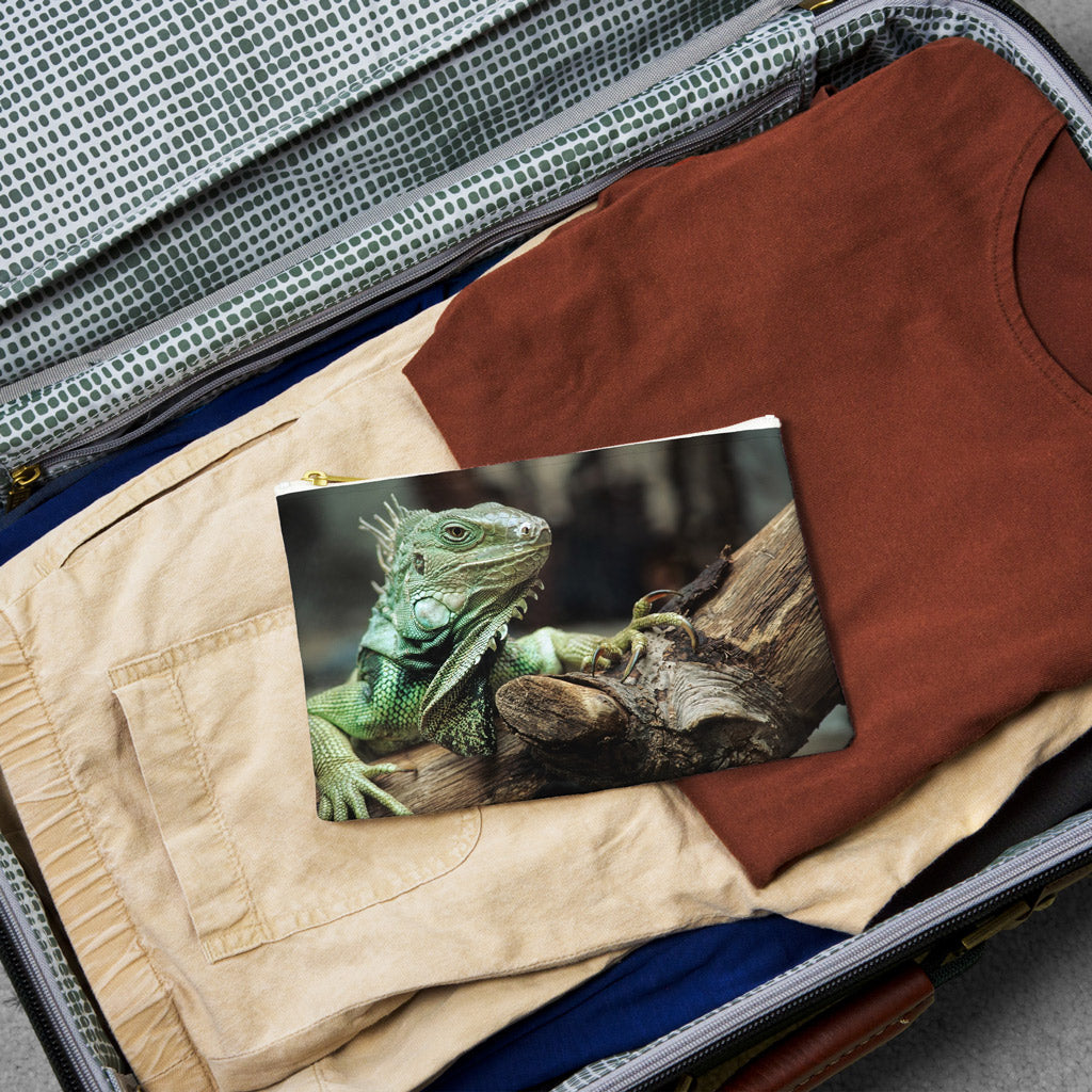 Small pouch with green iguana design lying flat atop the contents of an open suitcase.