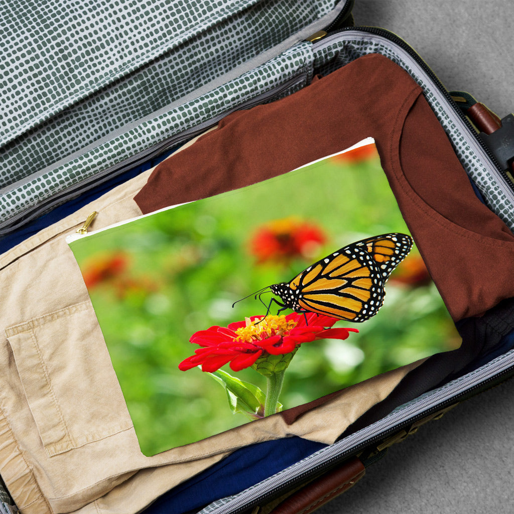 Large pouch with butterfly on flower design lying flat atop the contents of an open suitcase.