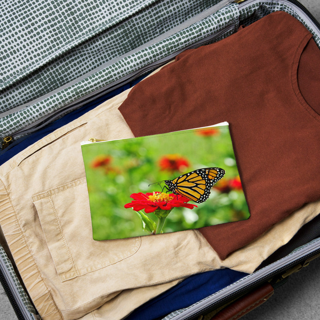 Small pouch with butterfly on flower design lying flat atop the contents of an open suitcase.