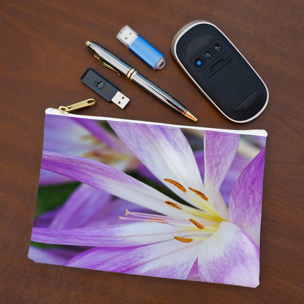 Small pouch with purple flower, orange stamen design lying flat on desktop with thumb drives, computer mouse and pen.