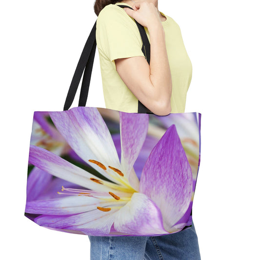 Young woman with a weekender bag featuring the purple flower, orange stamen design hanging from her shoulder.