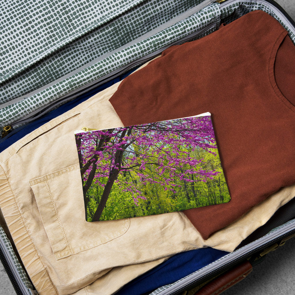Small pouch with tree blossoms design lying flat atop the contents of an open suitcase.