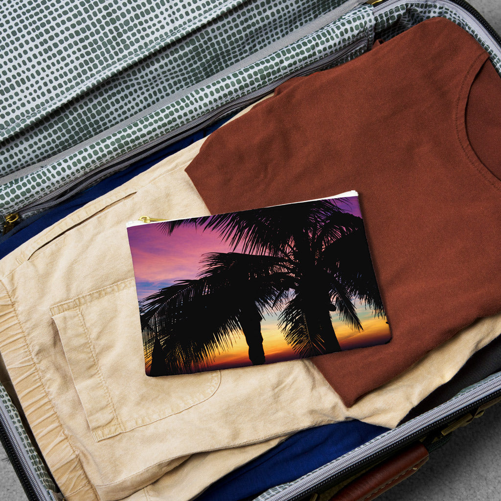 Small pouch with intense sunset design lying flat atop the contents of an open suitcase.