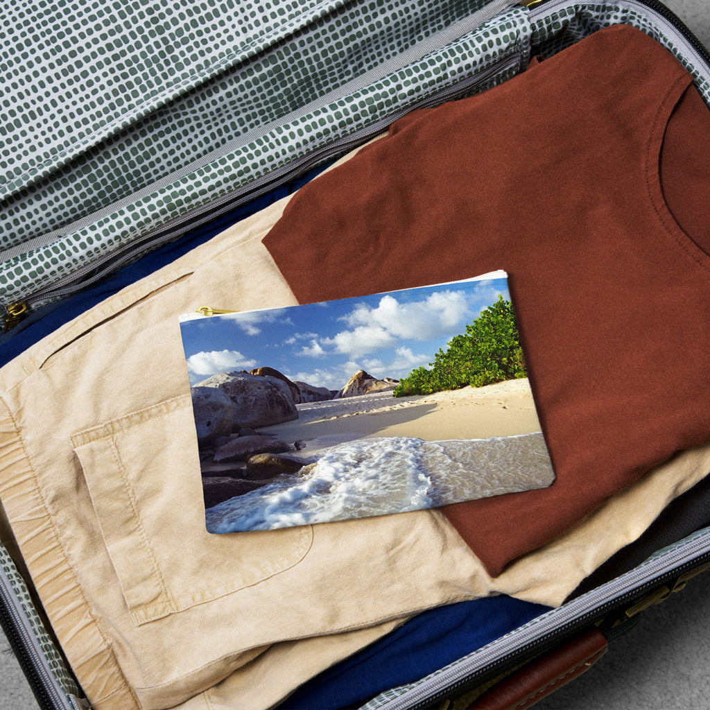 Small pouch with beach surf design lying flat atop the contents of an open suitcase.