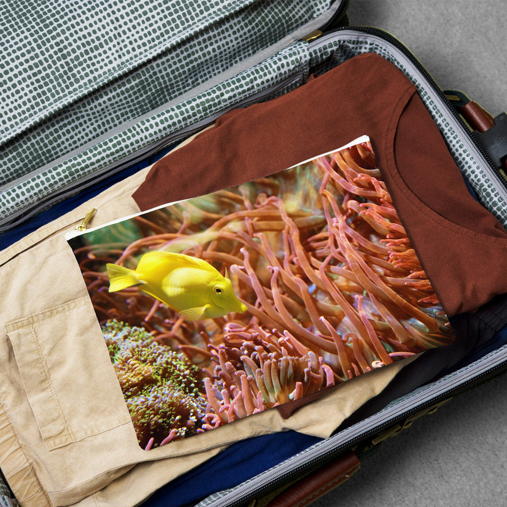 Large pouch with yellow fish design lying flat atop the contents of an open suitcase.