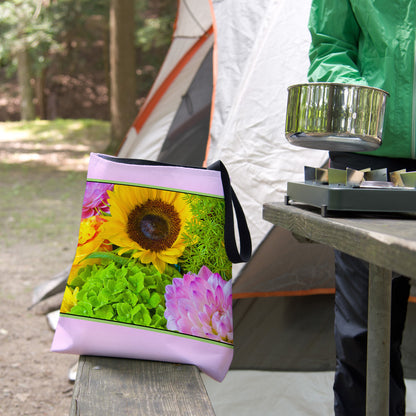 A tote bag featuring the flower bouquet design sits on the bench of a campsite picnic table as the camper cooks.
