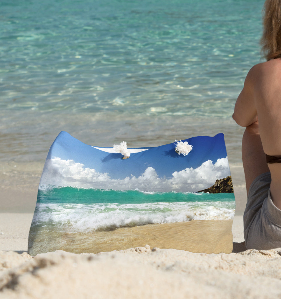 A young woman sitting on the beach with the crashing waves design beach bag by her side.