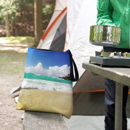 A tote bag featuring the crashing waves design sits on the bench of a campsite picnic table as the camper cooks.