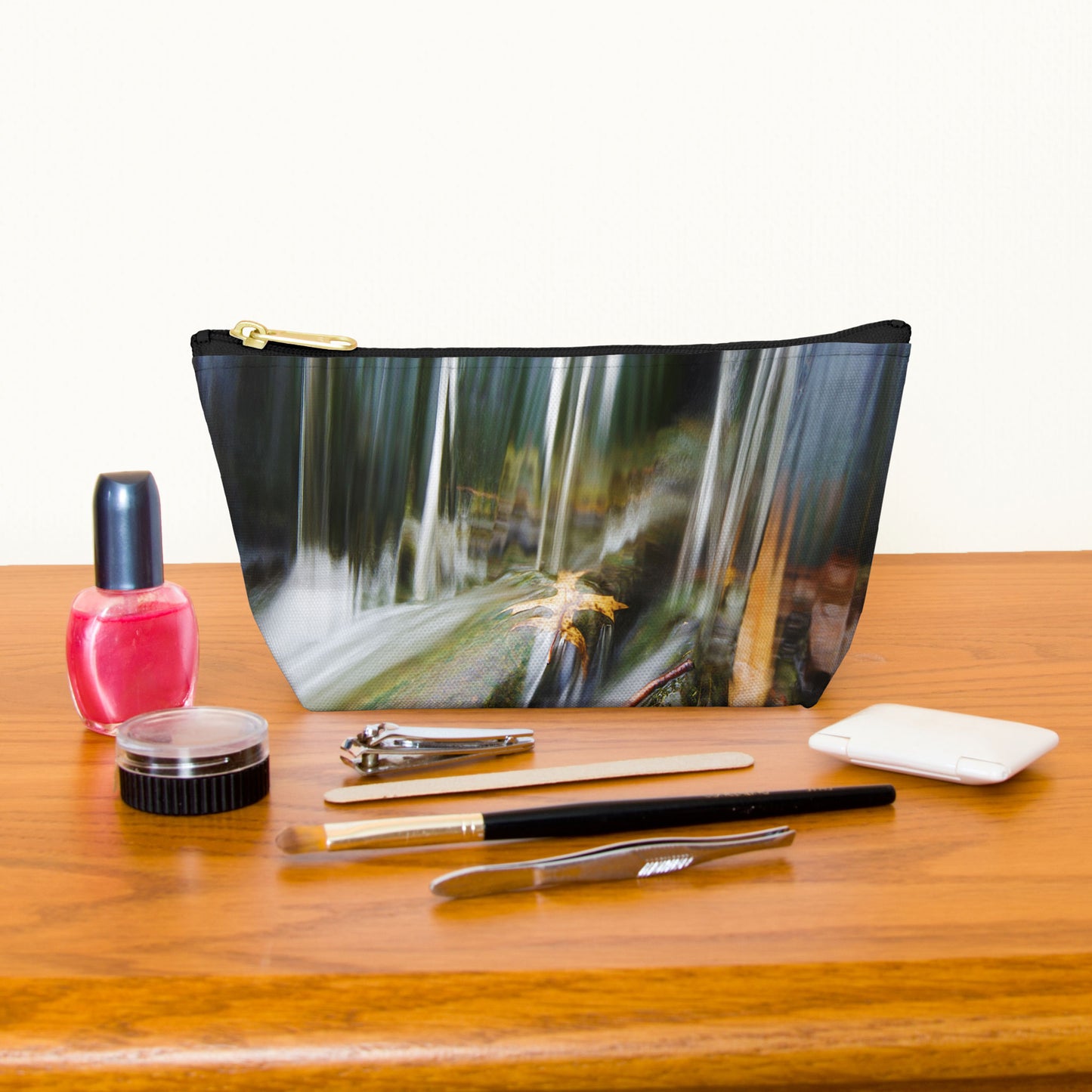 Kit bag with creek waterfall design next to nail polish, tweezers, nail clippers, makeup brush, blush and eye shadow.