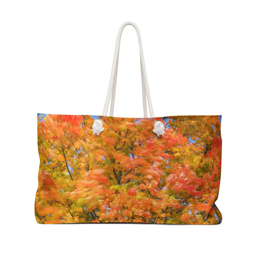 Front view of a beach bag featuring vibrant photo art of intense fall colored trees swaying wildly in a gusty wind.