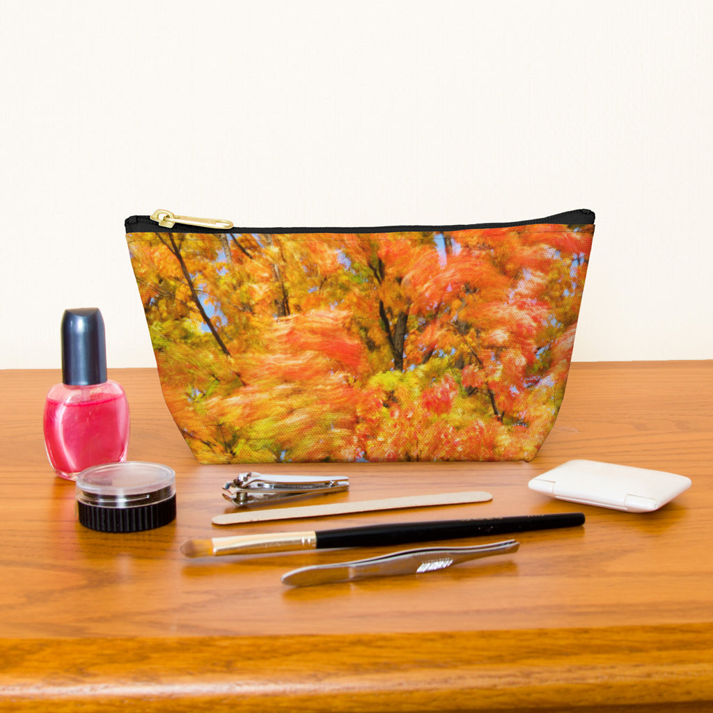 Kit bag with fall colored trees design next to nail polish, tweezers, nail clippers, makeup brush, blush and eye shadow.