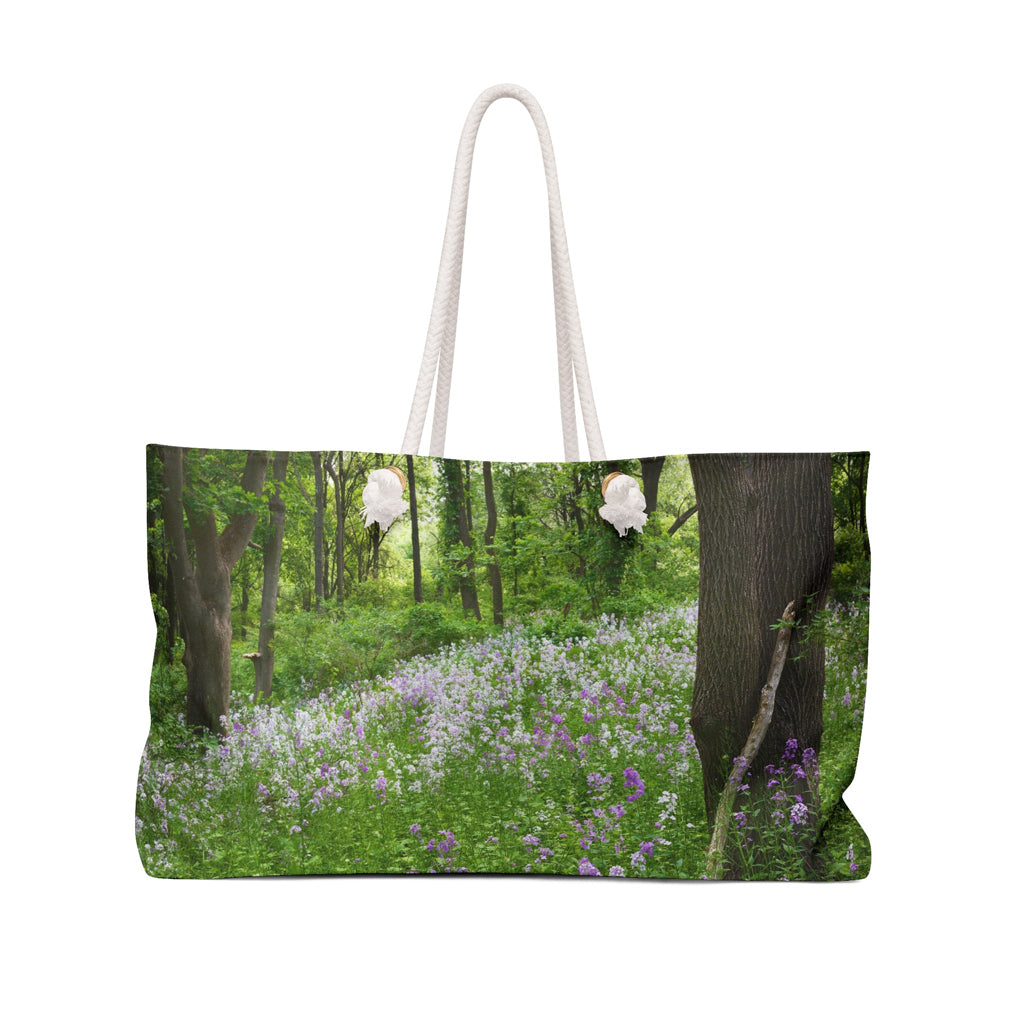 Front view of a beach bag featuring vibrant photo art of a forest hillside filled with lilac colored wildflowers.