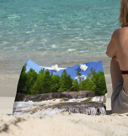 A young woman sitting on the beach with the forest waterfall design beach bag by her side.