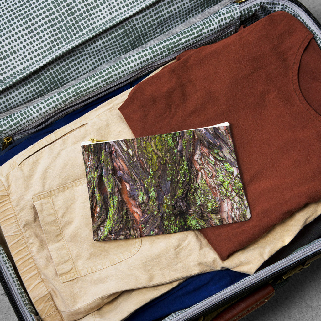 Small pouch with green mossy bark design lying flat atop the contents of an open suitcase.