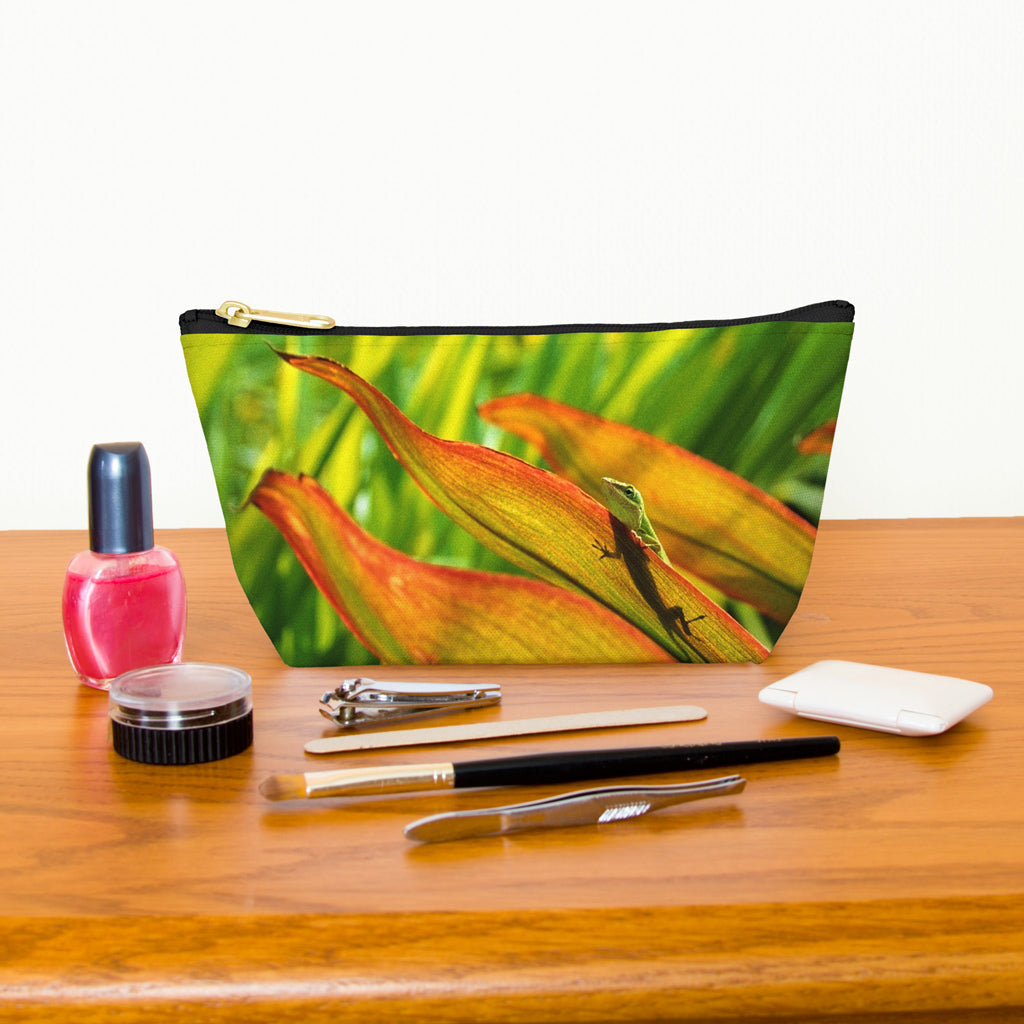 Kit bag with sunlit green gecko design next to nail polish, tweezers, nail clippers, makeup brush, blush and eye shadow.