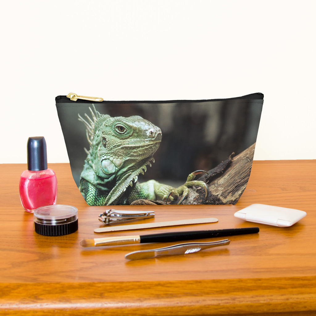 Kit bag with green iguana design next to nail polish, tweezers, nail clippers, makeup brush, blush and eye shadow.