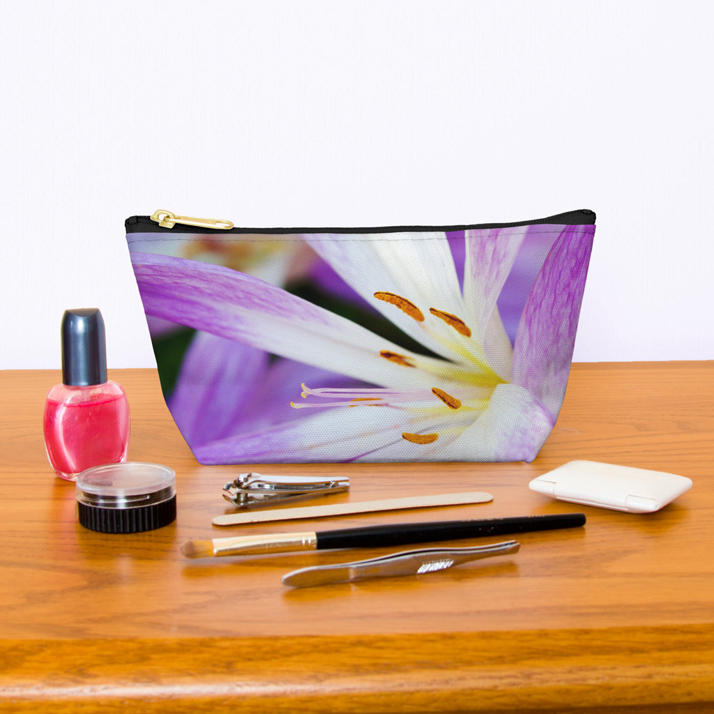 Kit bag with purple flower, orange stamen design next to nail polish, tweezers, nail clippers, makeup brush, blush and eye shadow.
