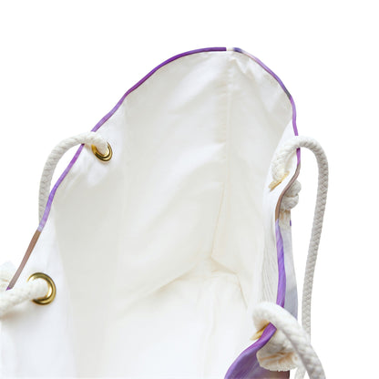 A close up view of the beach bag with purple flowers, orange stamen design shows the braided rope handles with metal grommets.