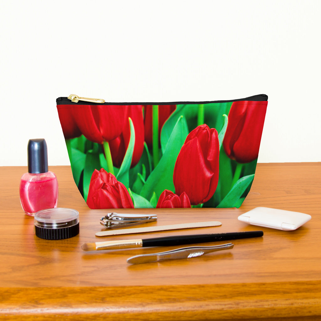 Kit bag with red tulips design next to nail polish, tweezers, nail clippers, makeup brush, blush and eye shadow.