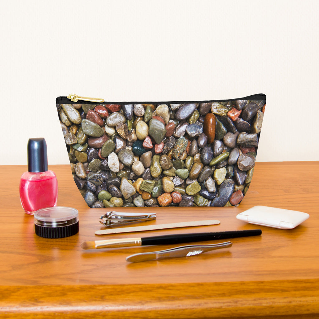 Kit bag with pebbles and stones design next to nail polish, tweezers, nail clippers, makeup brush, blush and eye shadow.