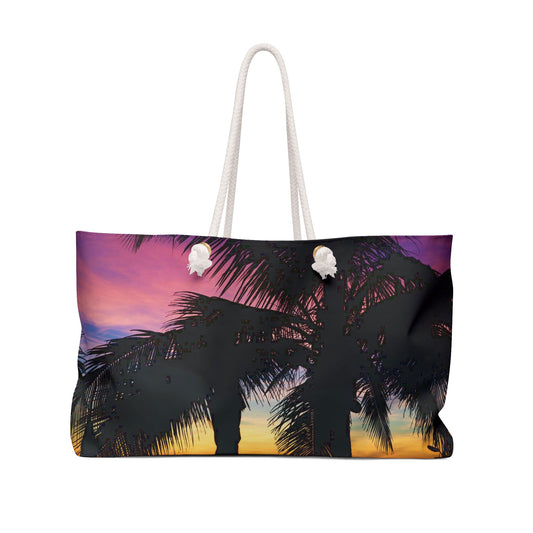 Front view of a beach bag featuring vibrant photo art of intense multi colored sunset with black palm trees in the foreground.