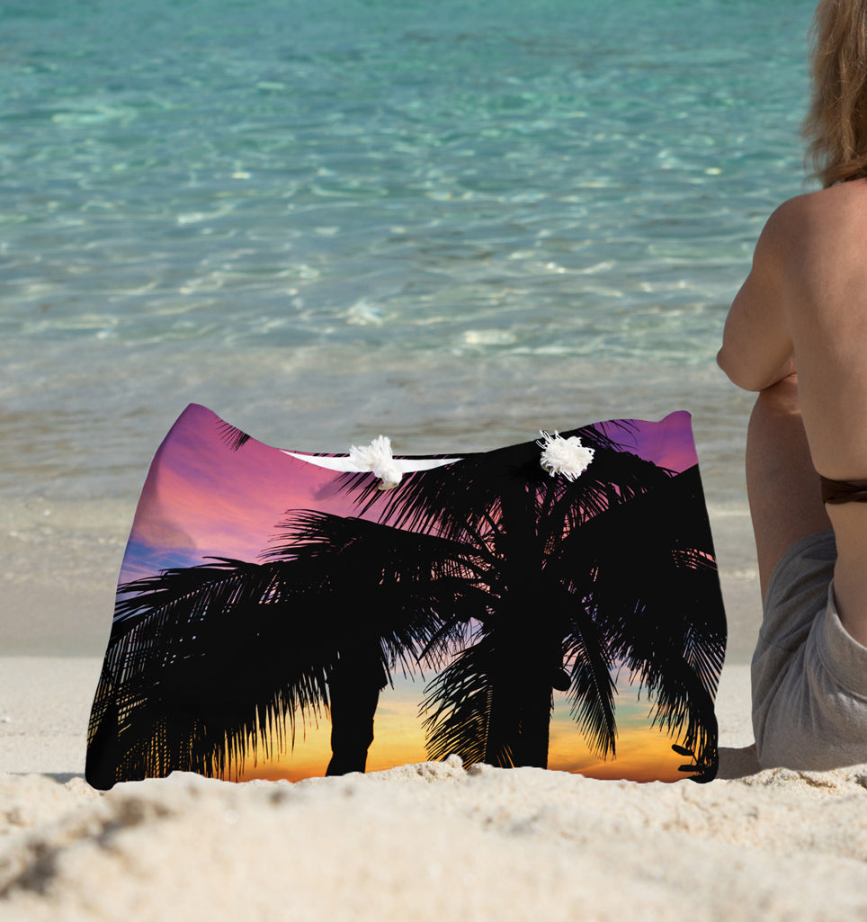 A young woman sitting on the beach with the intense sunset design beach bag by her side.