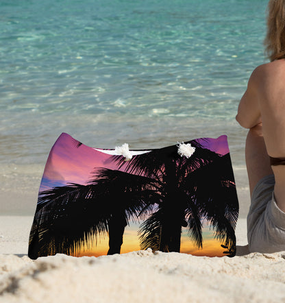 A young woman sitting on the beach with the intense sunset design beach bag by her side.