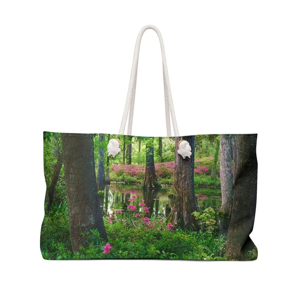 Front view of a beach bag featuring vibrant photo art of lush green trees and hot pink colored flowers in a Southern wetland.
