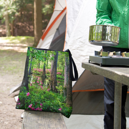 A tote bag featuring the wetland design sits on the bench of a campsite picnic table as the camper cooks.
