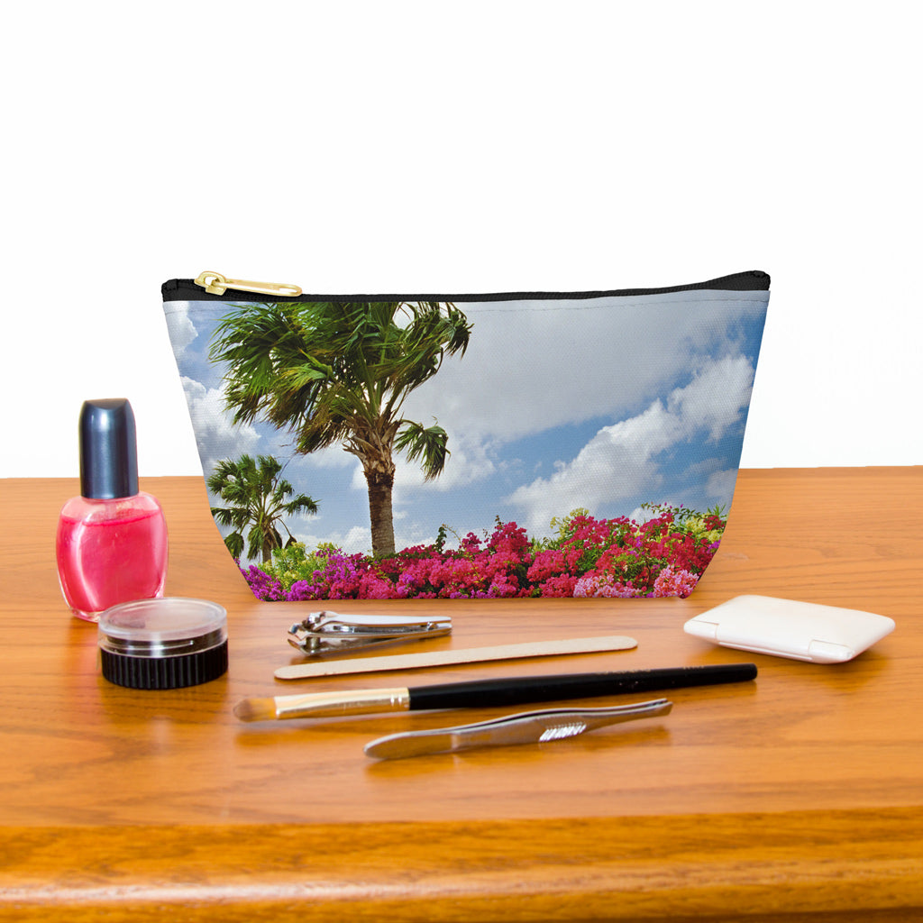 Kit bag with tropical flowers design next to nail polish, tweezers, nail clippers, makeup brush, blush and eye shadow.