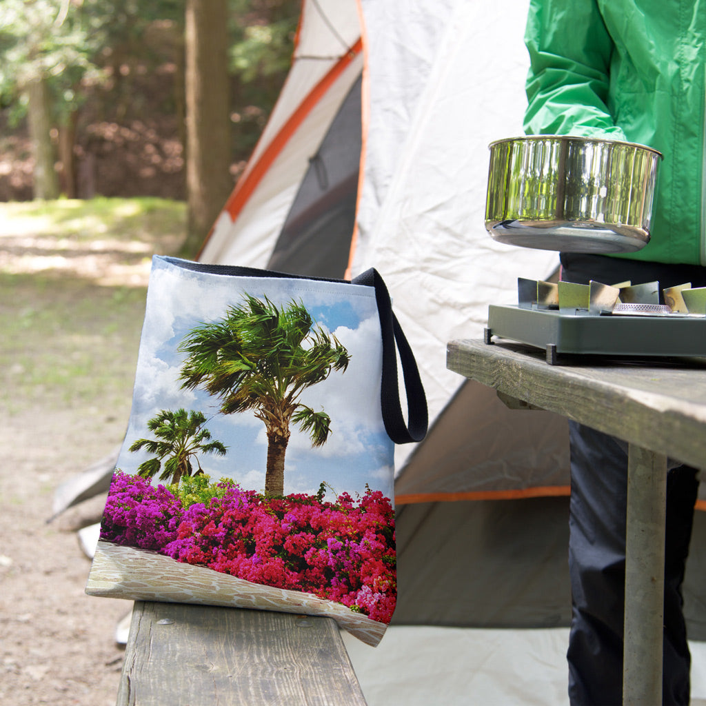 A tote bag featuring the tropical flowers design sits on the bench of a campsite picnic table as the camper cooks.