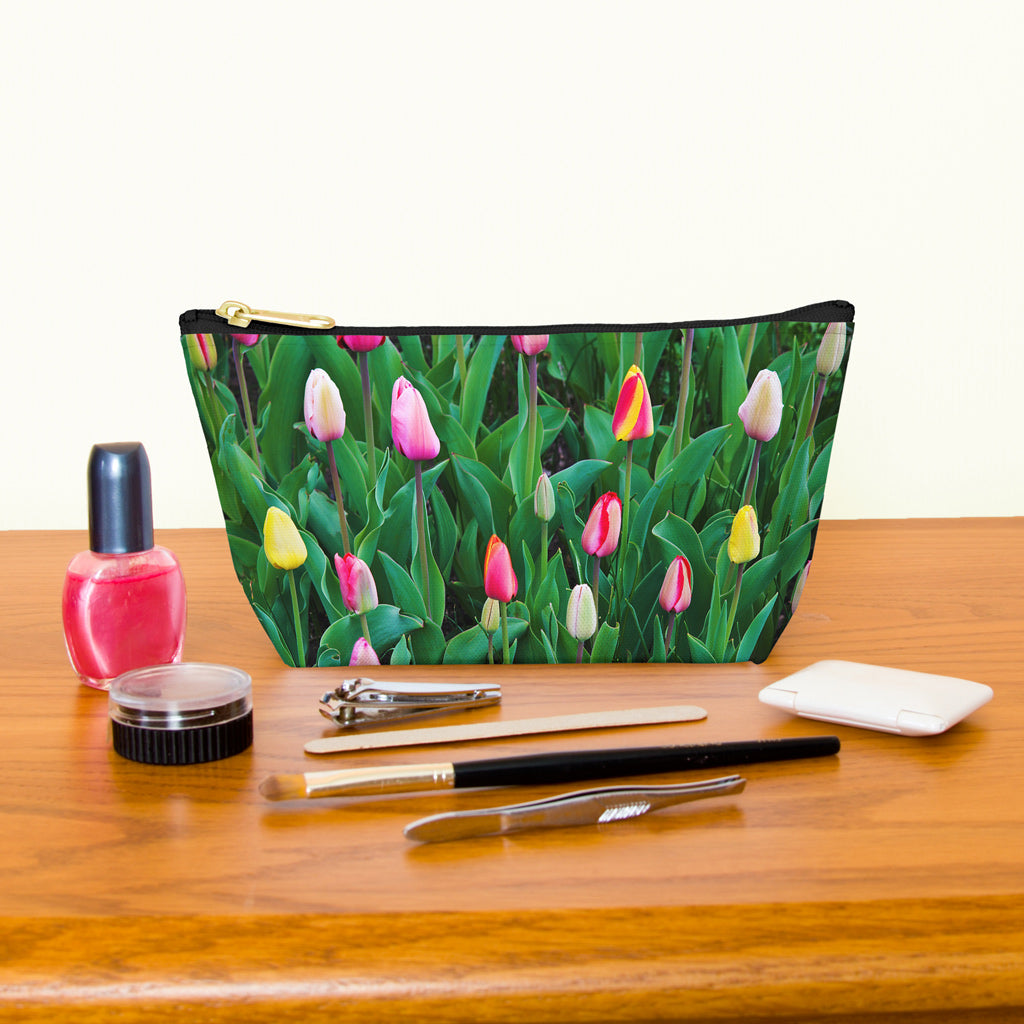 Kit bag with multi colored tulips design next to nail polish, tweezers, nail clippers, makeup brush, blush and eye shadow.