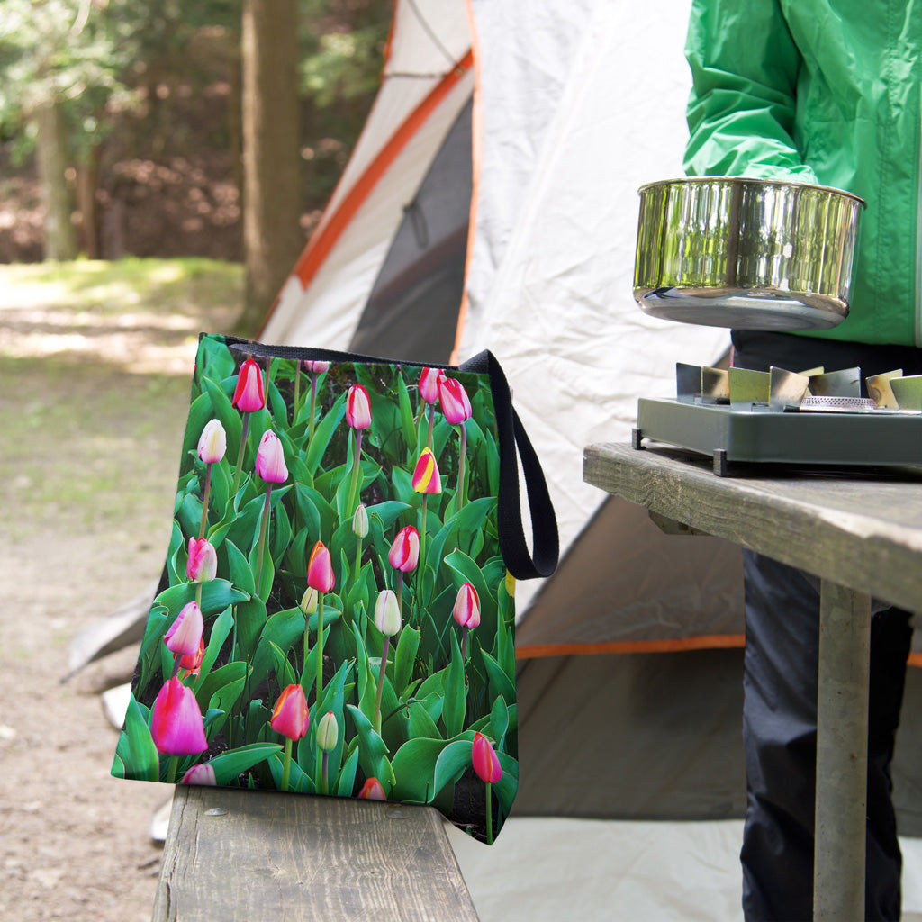 A tote bag featuring the multi colored tulips design sits on the bench of a campsite picnic table as the camper cooks.