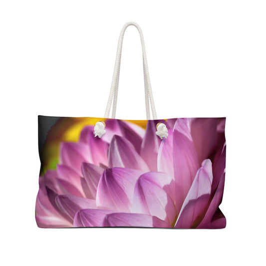 Front view of a beach bag featuring a vibrant photo art close up of pinkish violet colored flower petals in warm sunset light.