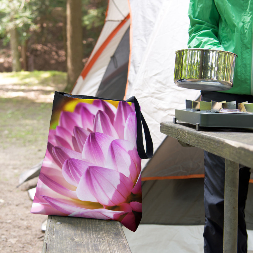 A tote bag featuring the flower petals design sits on the bench of a campsite picnic table as the camper cooks.